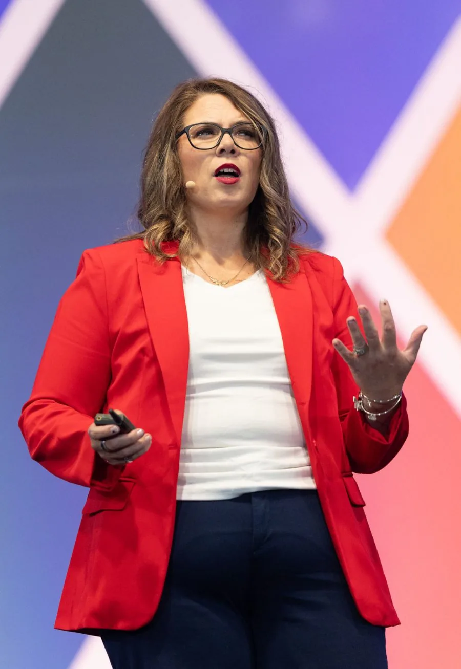 Kristi Jencks speaking on stage in a red blazer